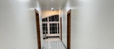 A hallway with white walls, a marble floor, and wooden doors.