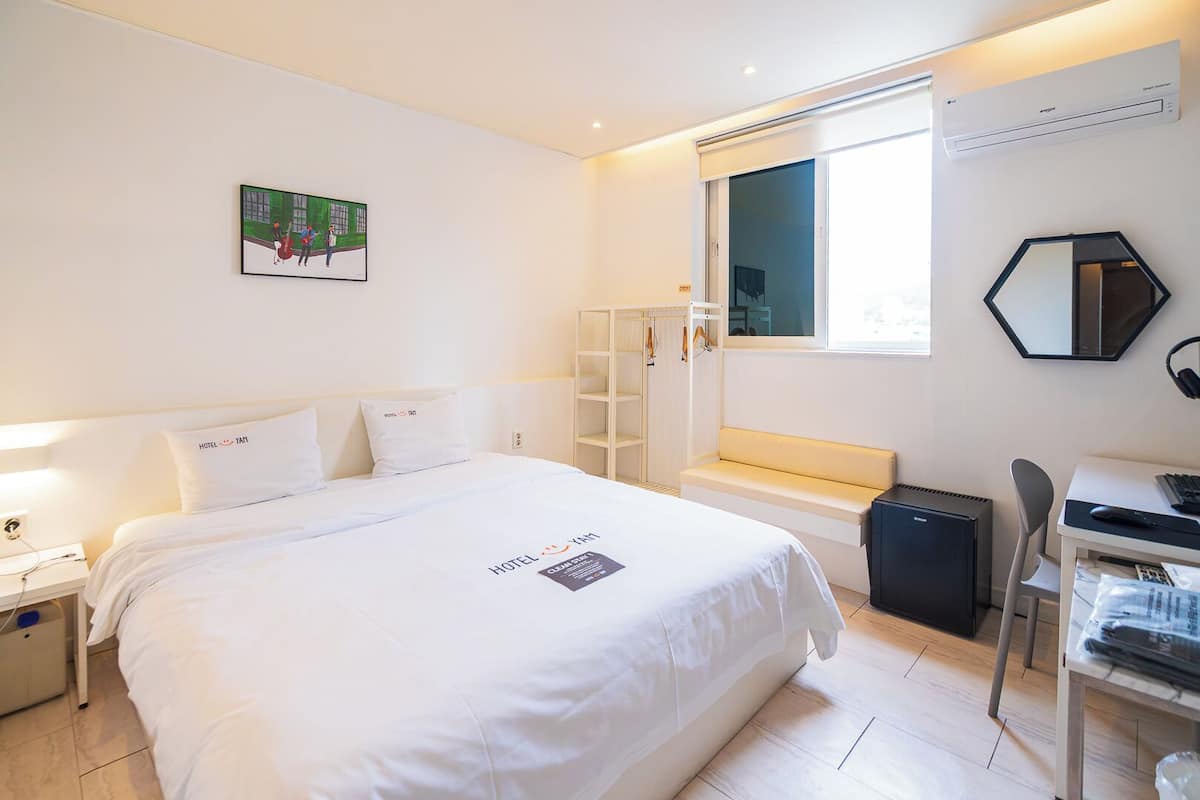 Una habitación de hotel con una cama, un escritorio con computadora, una ventana y un armario.