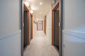 Un couloir d’hôtel avec des portes, un sol carrelé et des luminaires encastrés.