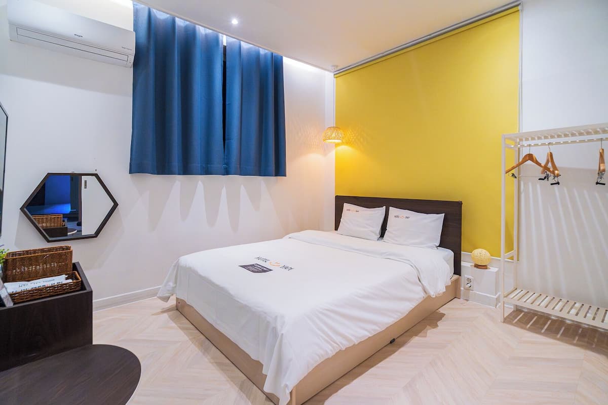 Una habitación de hotel con cama, espejo, mesita de noche, lámpara y armario.