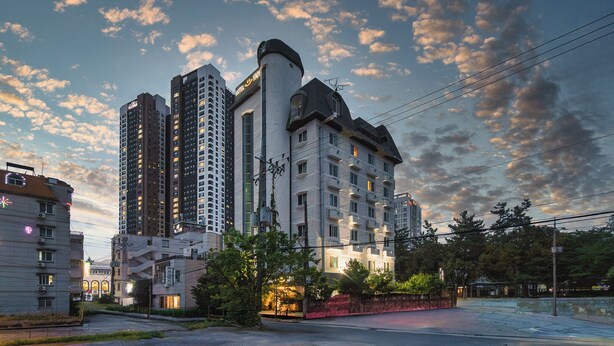Ein mehrstöckiges Hotel mit einem markanten Turm, umgeben von anderen Gebäuden und Bäumen.