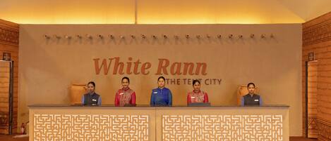 Una reception con una insegna che riporta "White Rann The Tenet City" e quattro membri dello staff seduti dietro.