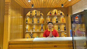 A bar area with wooden shelves stocked with various liquor bottles and glasses, a Pepsi refrigerator, and a bar counter. - Hotel Insta (Kathmandu)