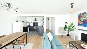 A modern living room with a sofa, dining table, and kitchen in the background. - Renovated apartment in Knokke-Heist with views (HEIST AAN ZEE)