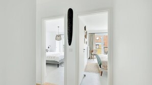 A hallway leading to a bedroom with a bed, a chair, and a decorative wall piece. - Renovated apartment in Knokke-Heist with views (HEIST AAN ZEE)