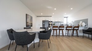Een moderne keuken met witte kasten, een roestvrijstalen koelkast, en een eetgedeelte met een marmeren tafel en zwarte stoelen.