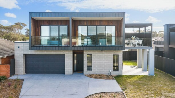Een modern huis met twee verdiepingen, een garage, grote ramen en een balkon.