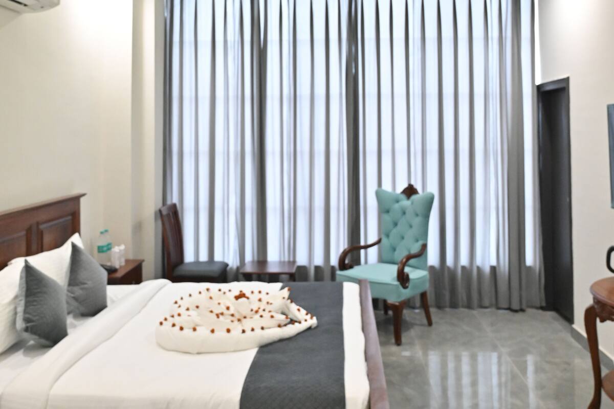 A modern bedroom with a bed, a chair, a ceiling fan, and a large window with curtains.