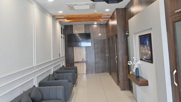 A modern hotel lobby with a long reception desk, grey sofas, and a large flat-screen TV on the wall. - Hotel Devaan (Bathinda)