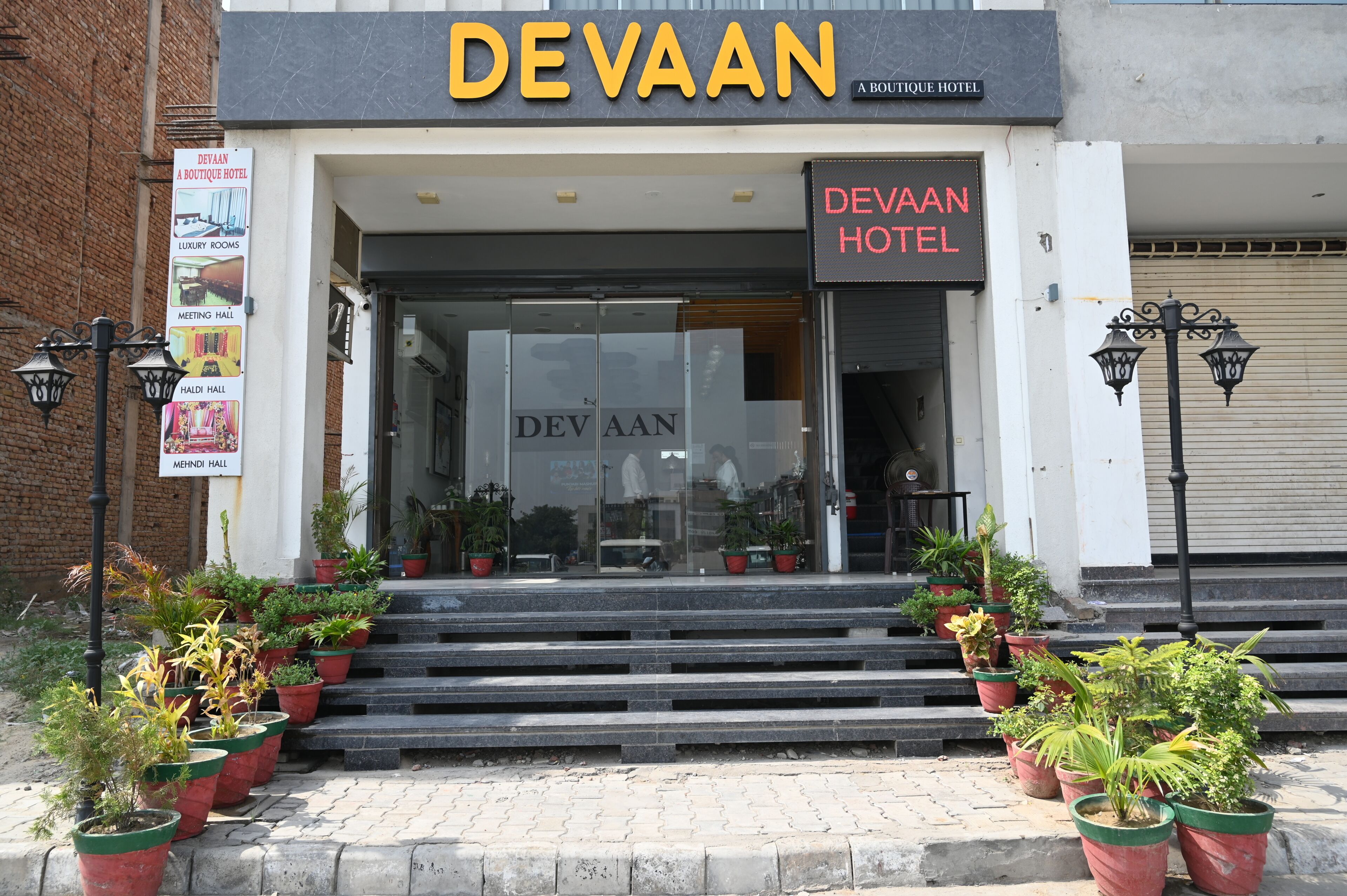 The entrance to Devaan Boutique Hotel with a glass facade, steps leading up to the entrance, and potted plants on the steps.