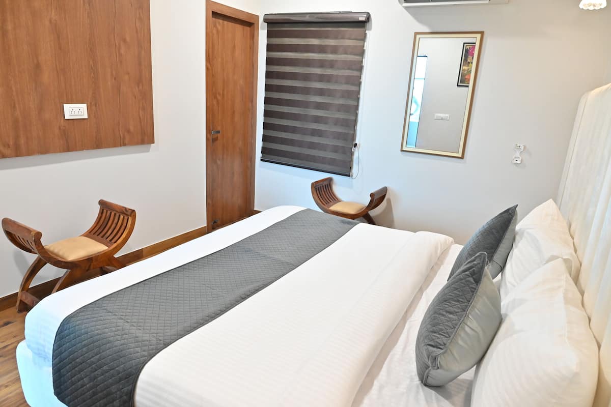 A bedroom with a bed, two wooden chairs, a window with a blind, a mirror, and a door.