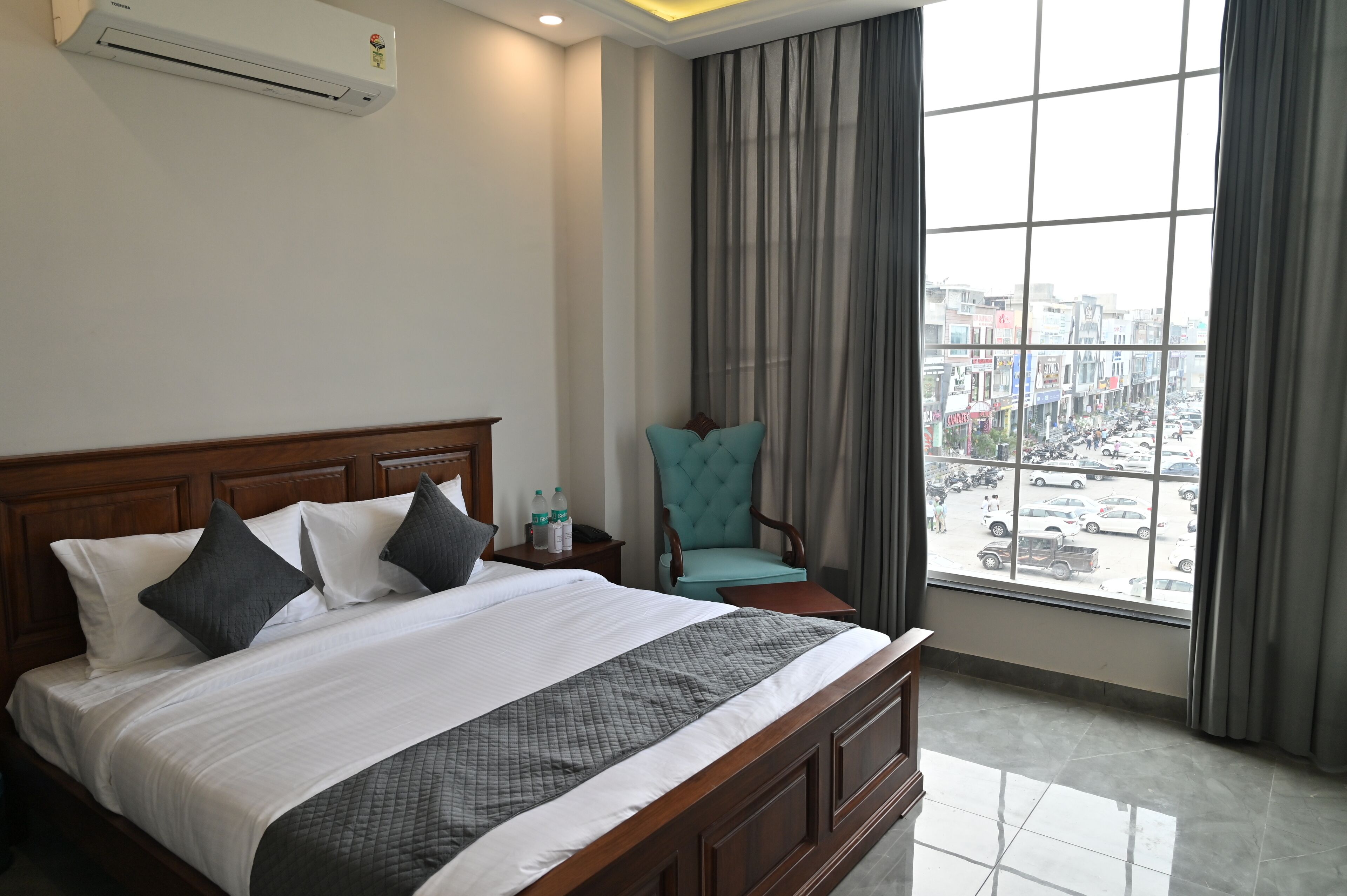 A hotel room with a large bed, a chair, a nightstand, and a view of the street through a window.