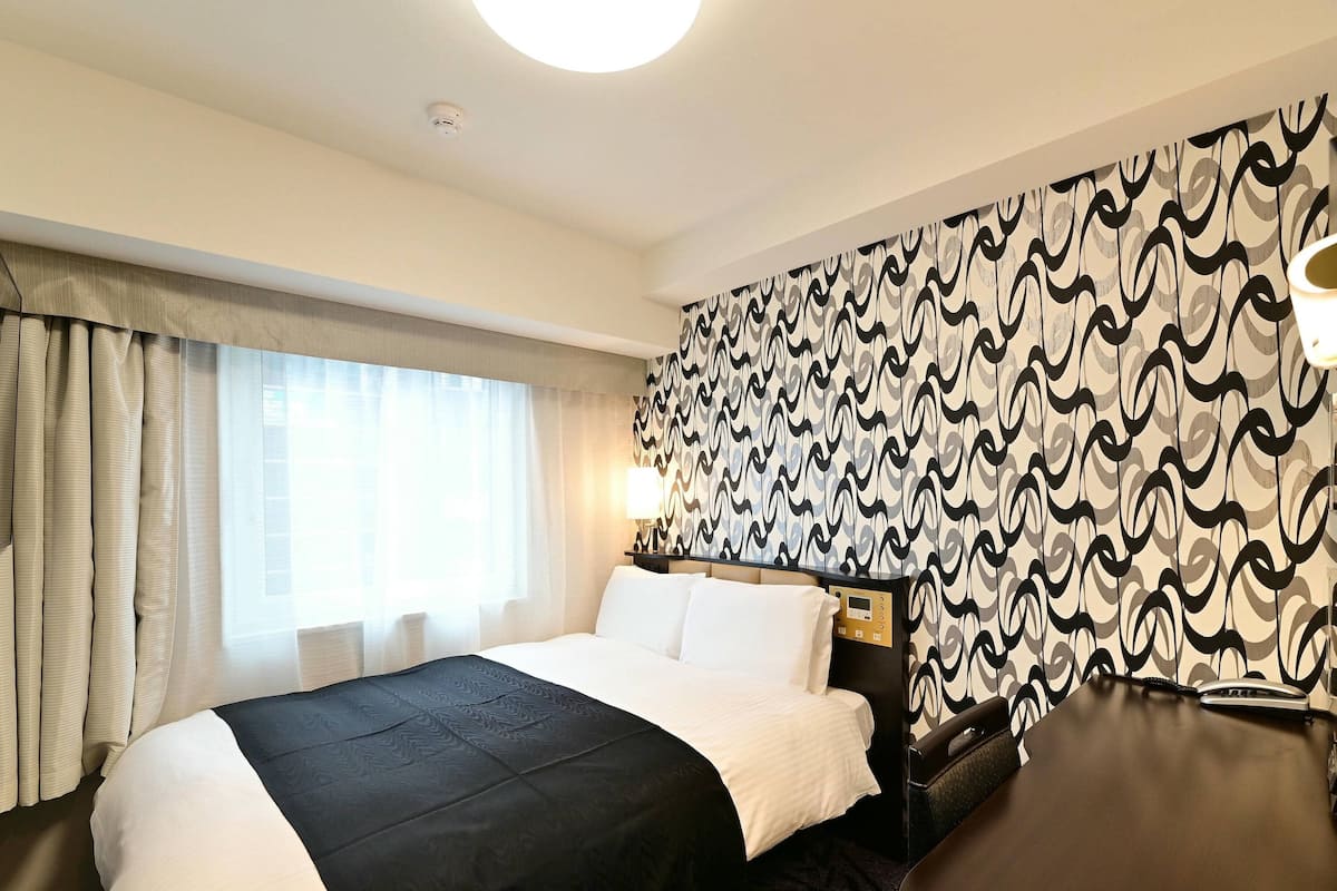Hotelkamer met een groot bed, een bureau, een stoel, een behang met patroon en een raam met gordijnen.