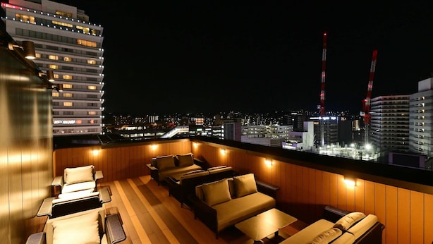 Un salon sur le toit doté de plusieurs espaces de détente, offrant une vue sur le paysage urbain, avec un bâtiment moderne en arrière-plan.