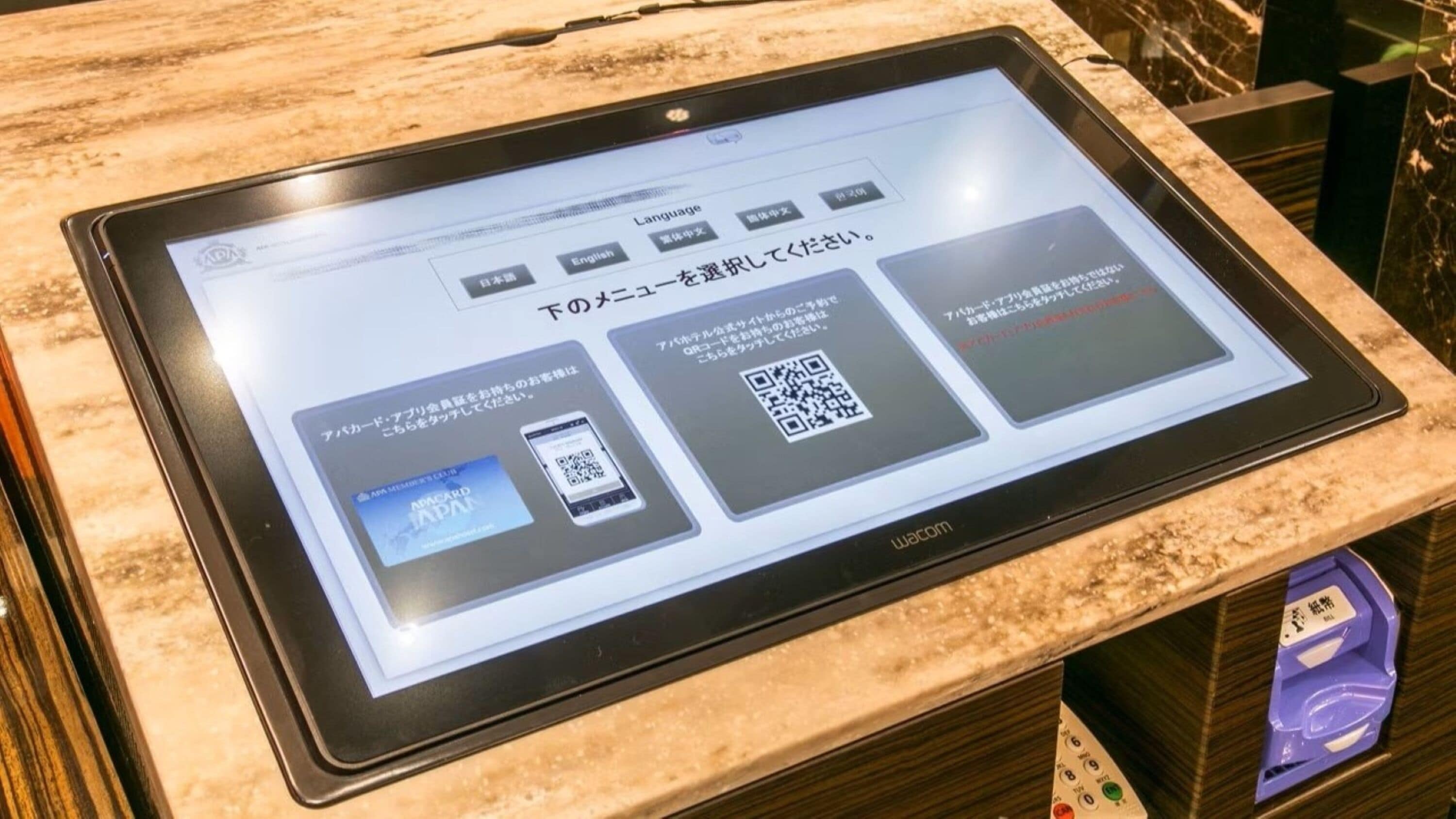 A digital kiosk with a screen displaying a QR code and text in Japanese, likely for hotel services or information.