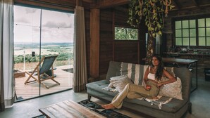 A cozy living room with a large window, a sofa, a coffee table, and a hanging plant. - Refugio Montevale - Cabana da Palmeira (Passo do Sobrado)