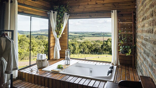 A wooden cabin with a large skylight, a bathtub, and a view of the countryside. - Refugio Montevale - Cabana da Palmeira (Passo do Sobrado)