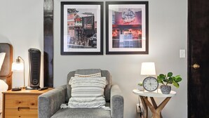 A gray armchair with a patterned throw, a small table with a clock and a plant, and two framed pictures on the wall. - The Classic City Collection - 3 Separate Units (Athens)