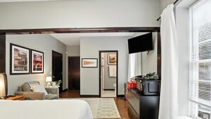 A hotel room with a bed, a desk, a chair, a TV, and a window with blinds. - The Classic City Collection - 3 Separate Units (Athens)