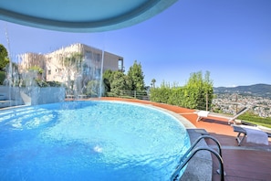 Ein Schwimmbecken mit Wasserfall, Liegestühlen und Blick auf Stadt und Berge.