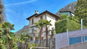 A multi-story building with balconies, surrounded by lush greenery and mountains in the background. - Oasis Panoramic 1BR With Shared Pool (Lugano)
