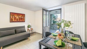 A living room with a sofa, a dining table set with a vase of flowers, and a view of the outside. - Oasis Panoramic 1BR With Shared Pool (Lugano)