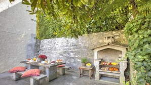 An outdoor patio with stone benches, a table set with food and drinks, and a stone wall. - Oasis Panoramic 1BR With Shared Pool (Lugano)