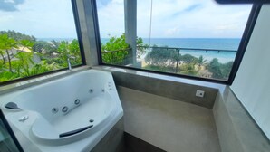 Un baño moderno con una bañera grande, vista al océano y un balcón con plantas.