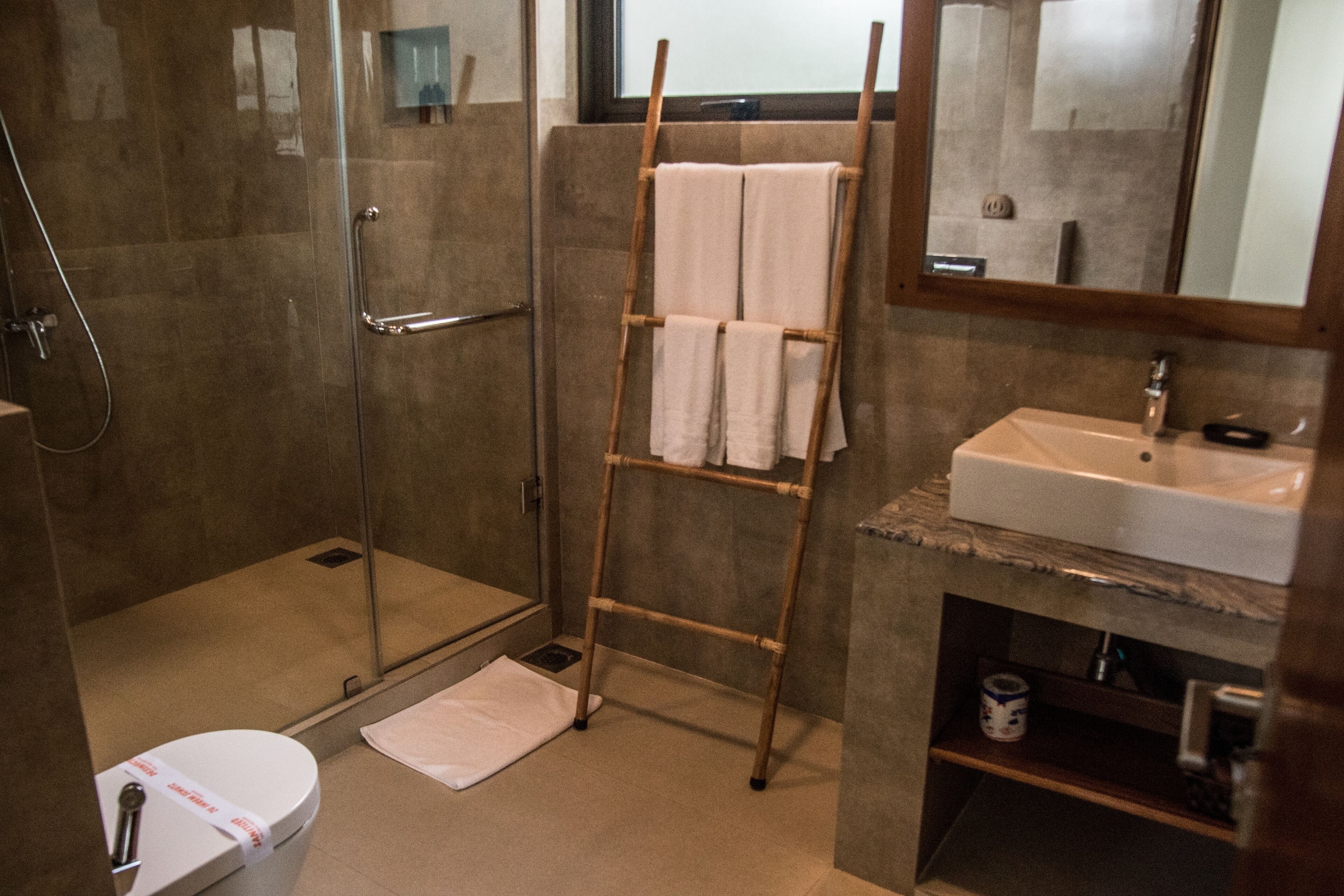 Une salle de bain moderne avec une douche à parois de verre, un porte-serviettes en bois, des toilettes blanches et un lavabo surmonté d’un plan de travail en marbre.