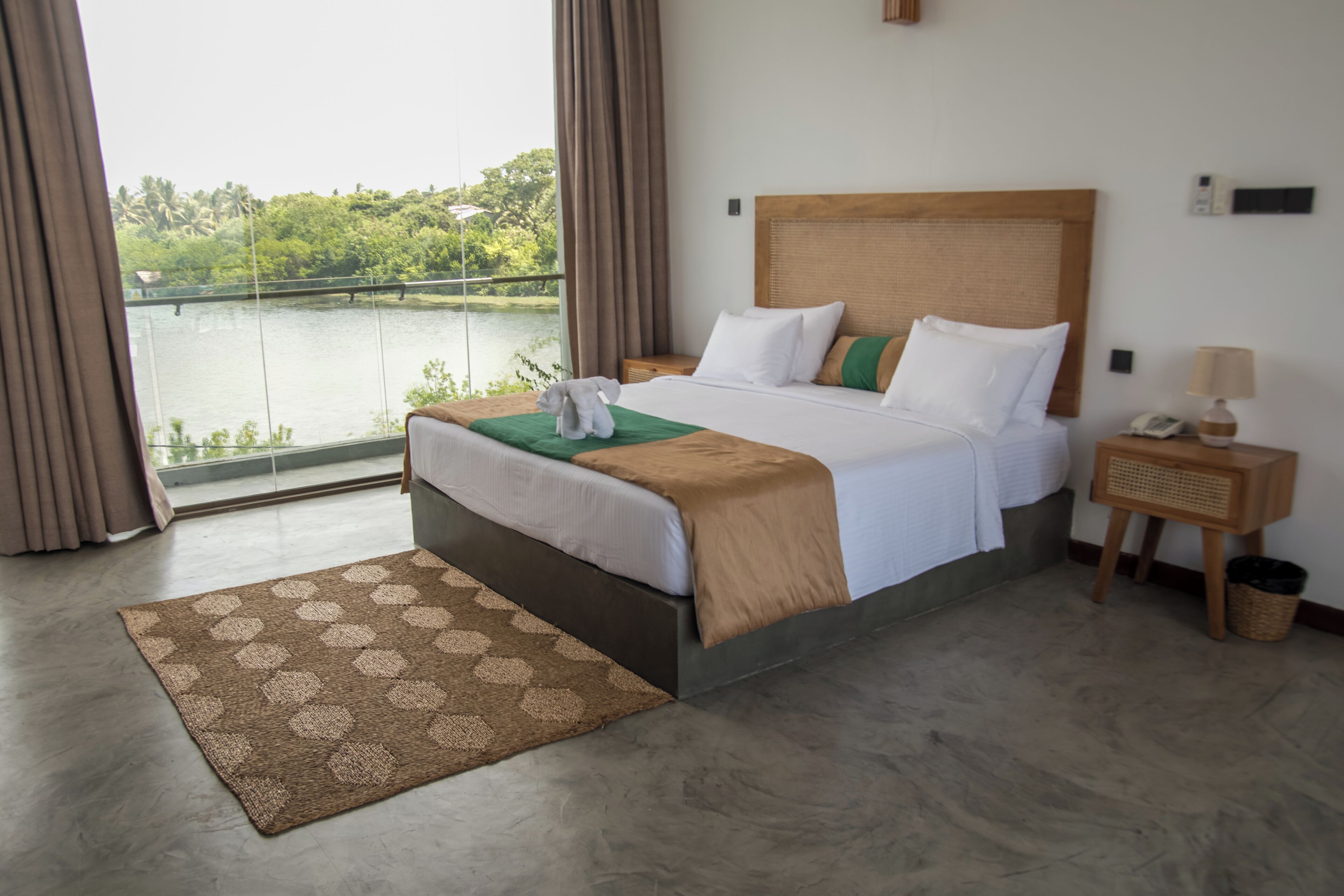 A hotel room with a large bed, a view of a lake, a wooden nightstand, and a small table with a lamp.