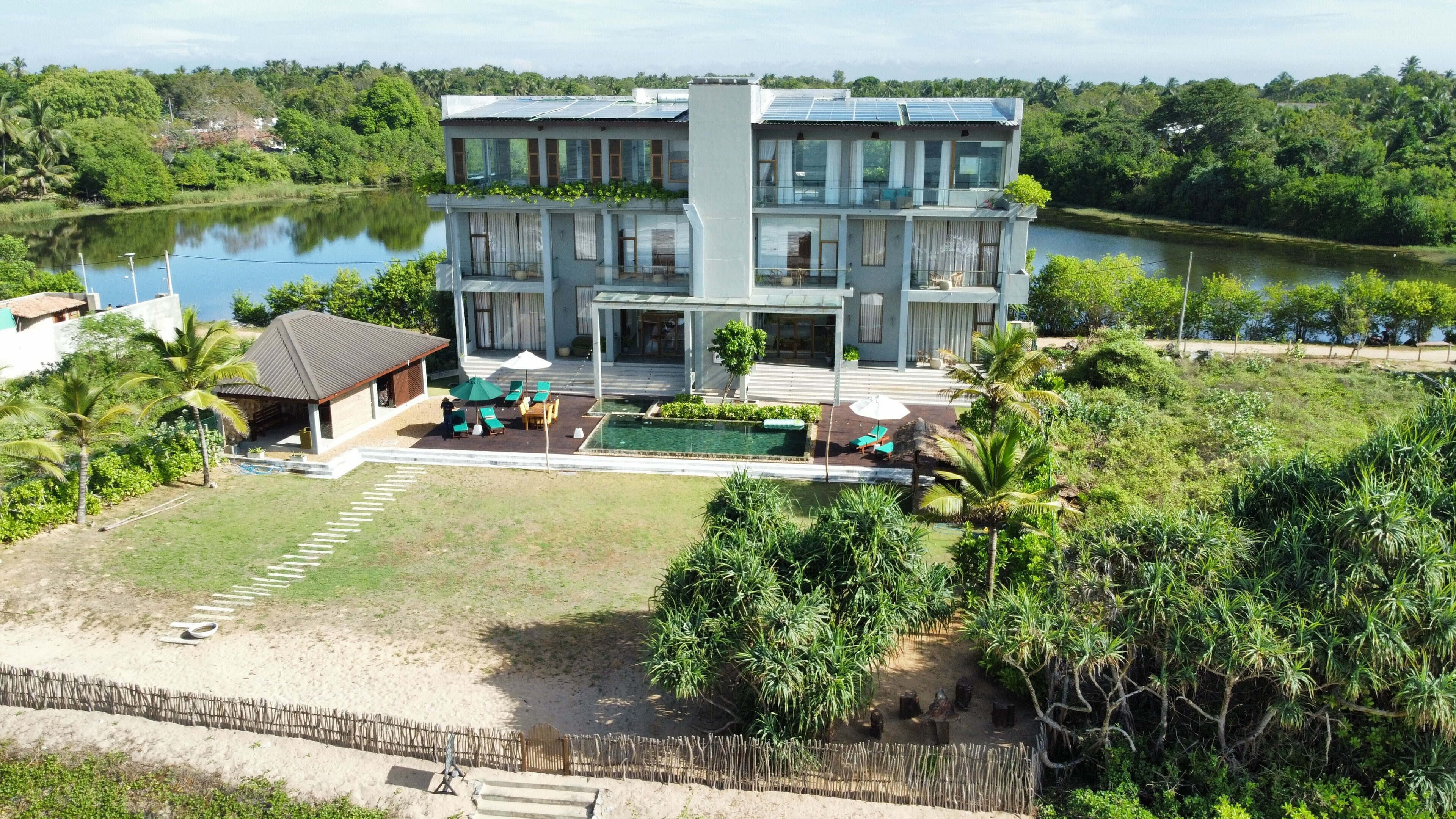Ein modernes, mehrgeschossiges Gebäude mit Schwimmbad, umgeben von üppiger Vegetation und einem See.