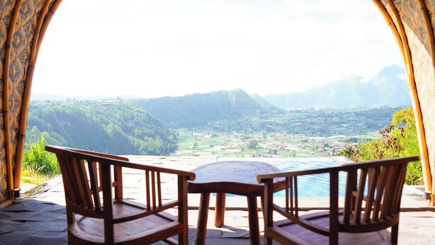 Una mesa y sillas de madera con vistas a un valle y montañas a través de un arco.