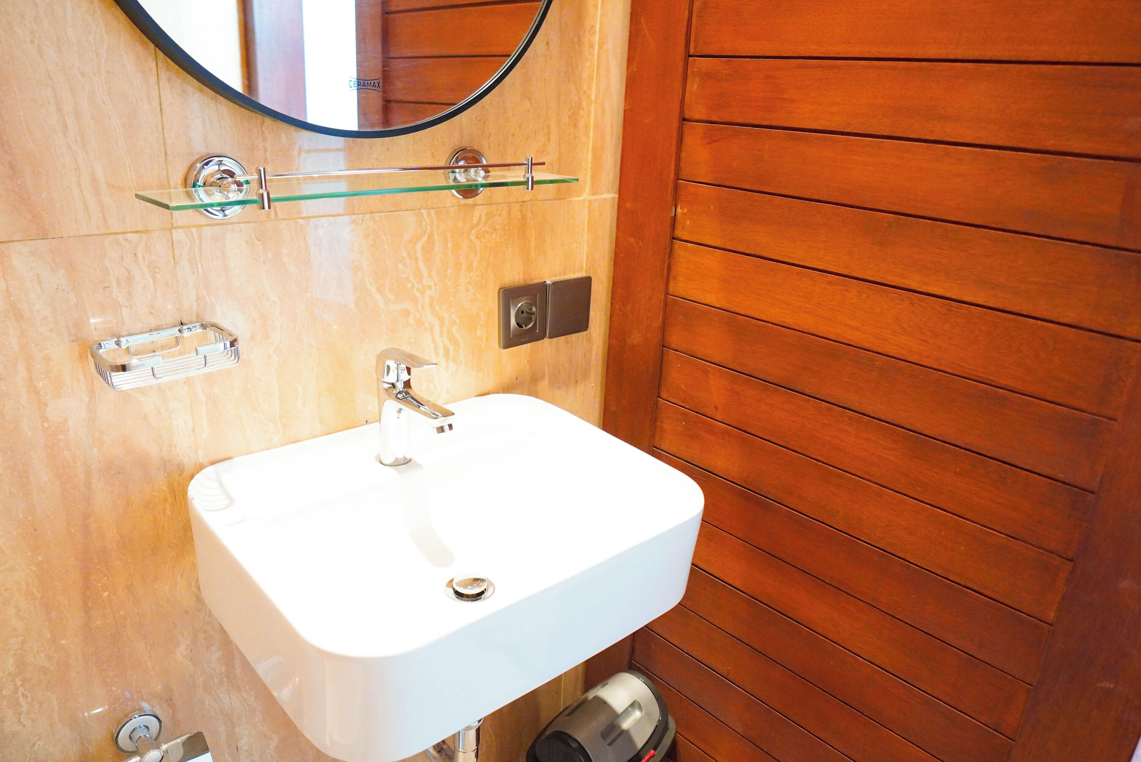 A bathroom with a white sink, a glass shelf above the sink, and a wooden wall.