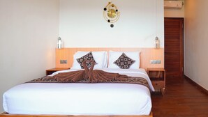 Una cama bien hecha con sábanas blancas y almohadas estampadas, un cabecero de madera y un reloj fijado a la pared.