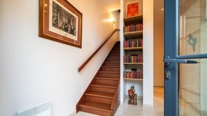A staircase leading to a landing with a framed historical photograph, a radiator, and a bookshelf with books and a small statue. - The Hôtel de Beaumont carriages (Valognes)