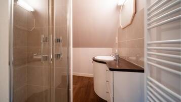 Ein Badezimmer mit einer Duschkabine aus Glas, einem weißen Waschbecken und einem Spiegel an der Wand.