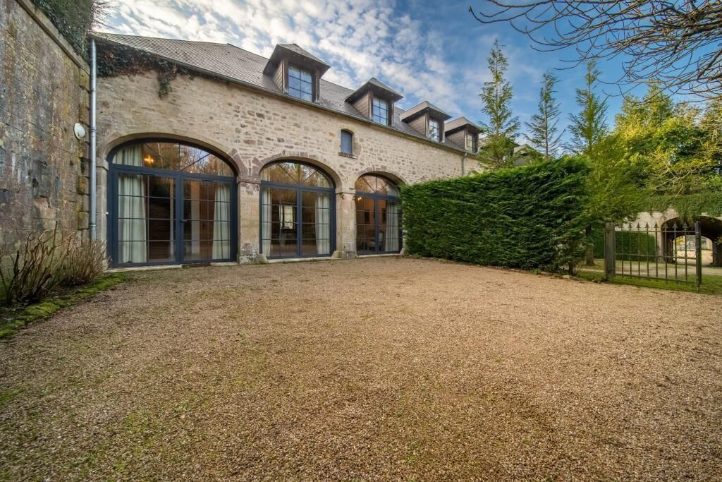A stone building with large arched windows and a gravel driveway.