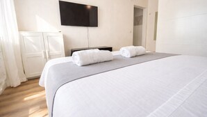 A hotel room with a large bed, two rolled towels, a flat-screen TV on the wall, a wardrobe, and a door leading to another room. - Nestop Colli Albani (Rome)