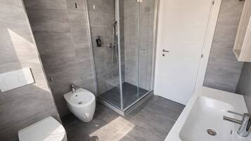 Un bagno moderno con doccia vetrata, bidet, water e vasca da bagno.
