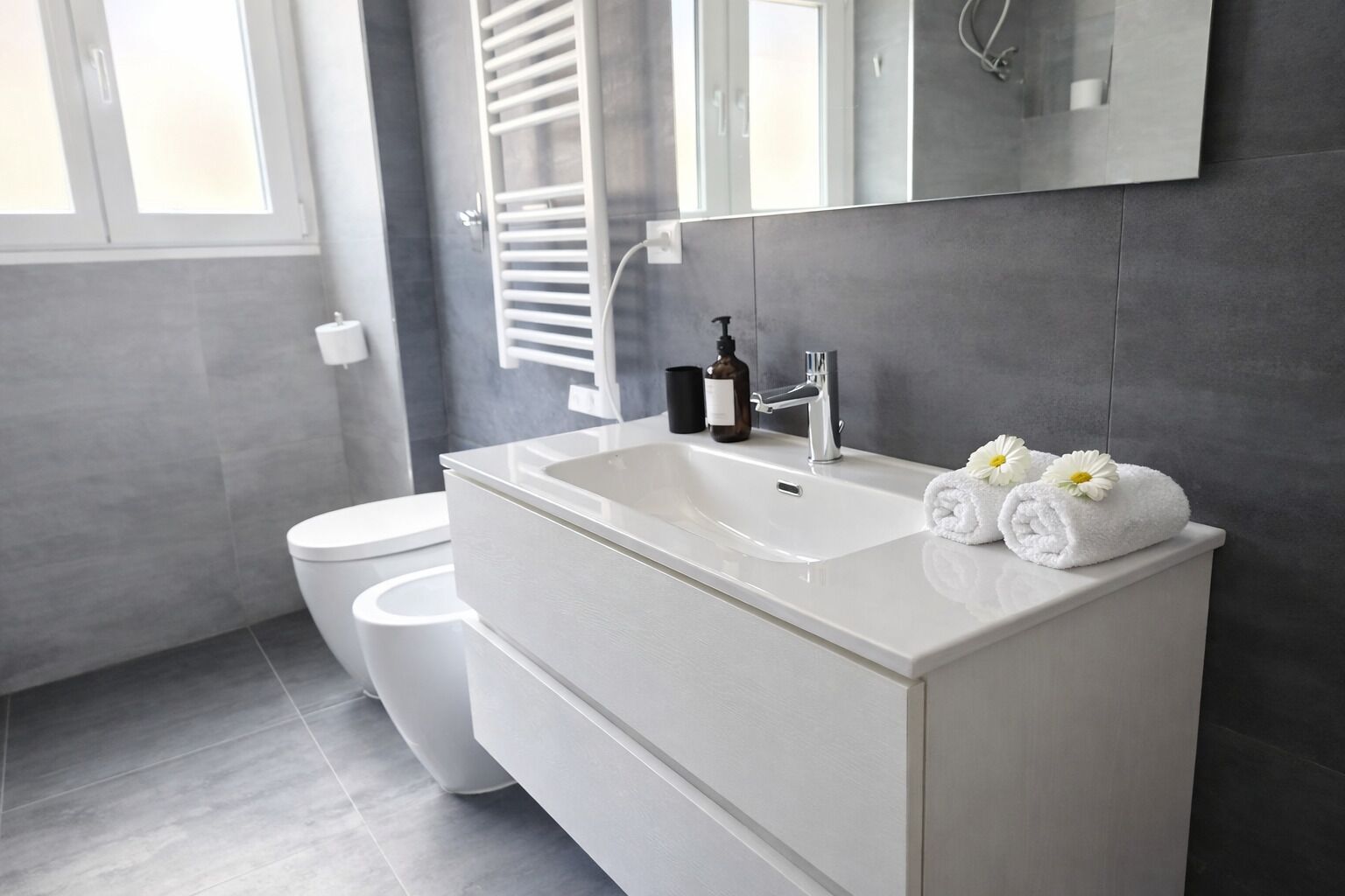 A modern bathroom with a white sink, a mirror, and a towel with flowers.