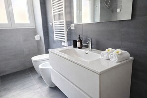 A modern bathroom with a white sink, a mirror, and a towel with flowers. - Casa Dolce Casa - Dual Modern Apartment  (Rome)