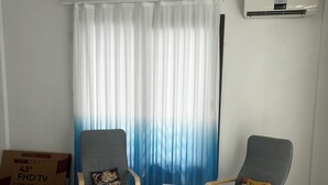Un salón con dos sillones grises, una mesita blanca y un ventanal con cortinas de gasa.