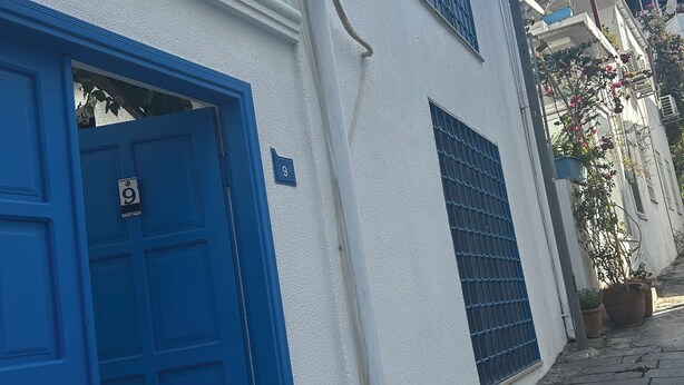 Un edificio blanco con puerta y contraventanas azules, adoquinado y cielo despejado.