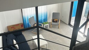 Una sala de estar moderna con un sofá, una mesa de centro y una silla. Una escalera conduce a un piso superior.