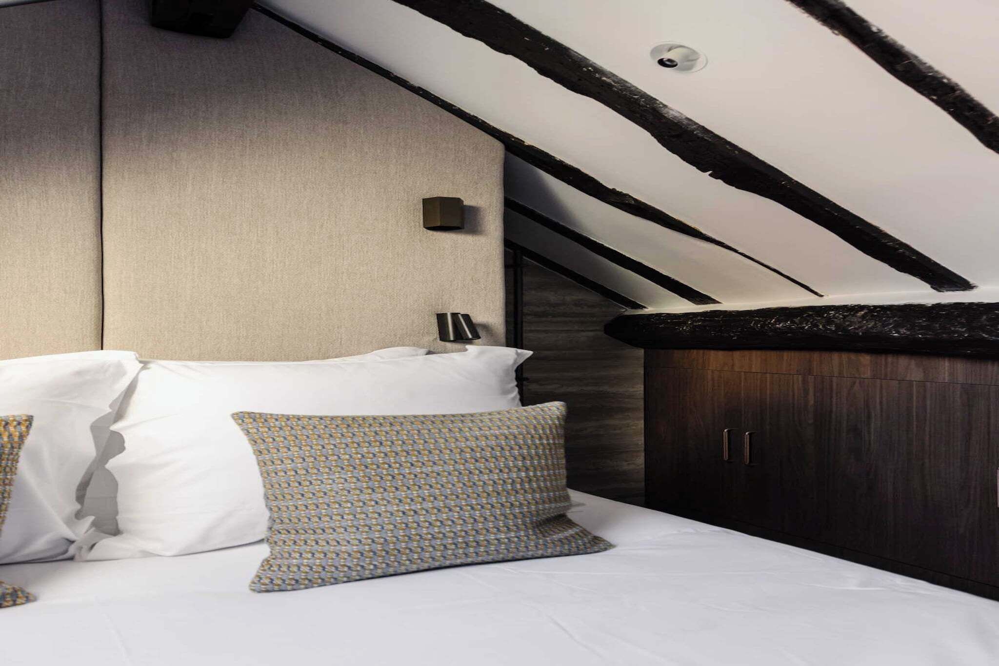 Ein Schlafzimmer mit Bett, Kissen, Kopfteil, Kleiderschrank und schrägen Wänden.