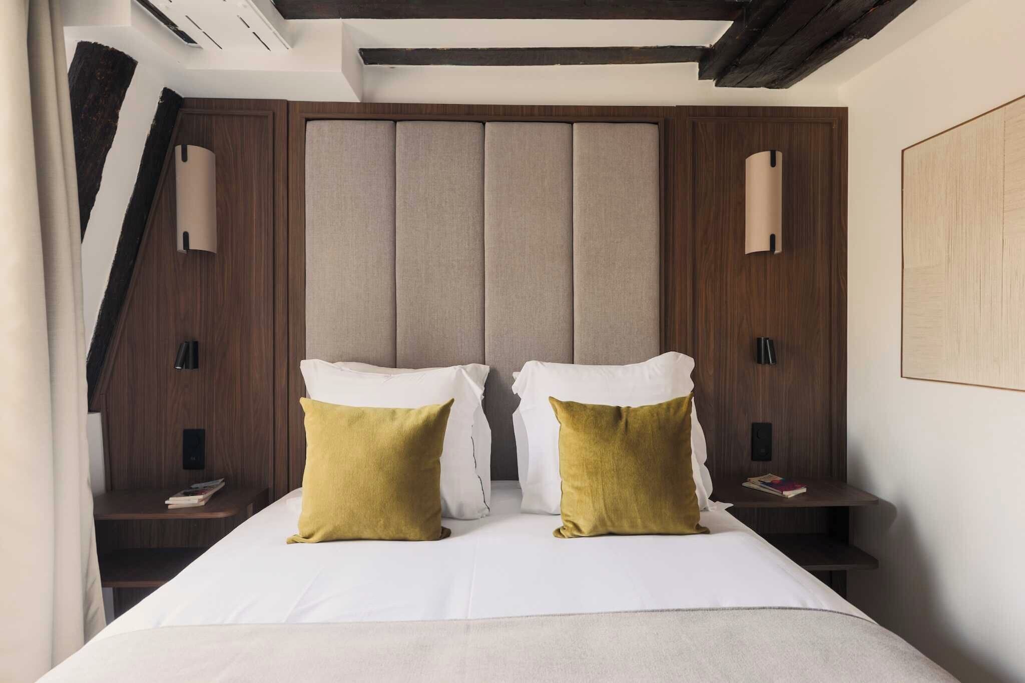 A hotel room with a bed, two bedside tables, a headboard, and a wall-mounted light fixture.
