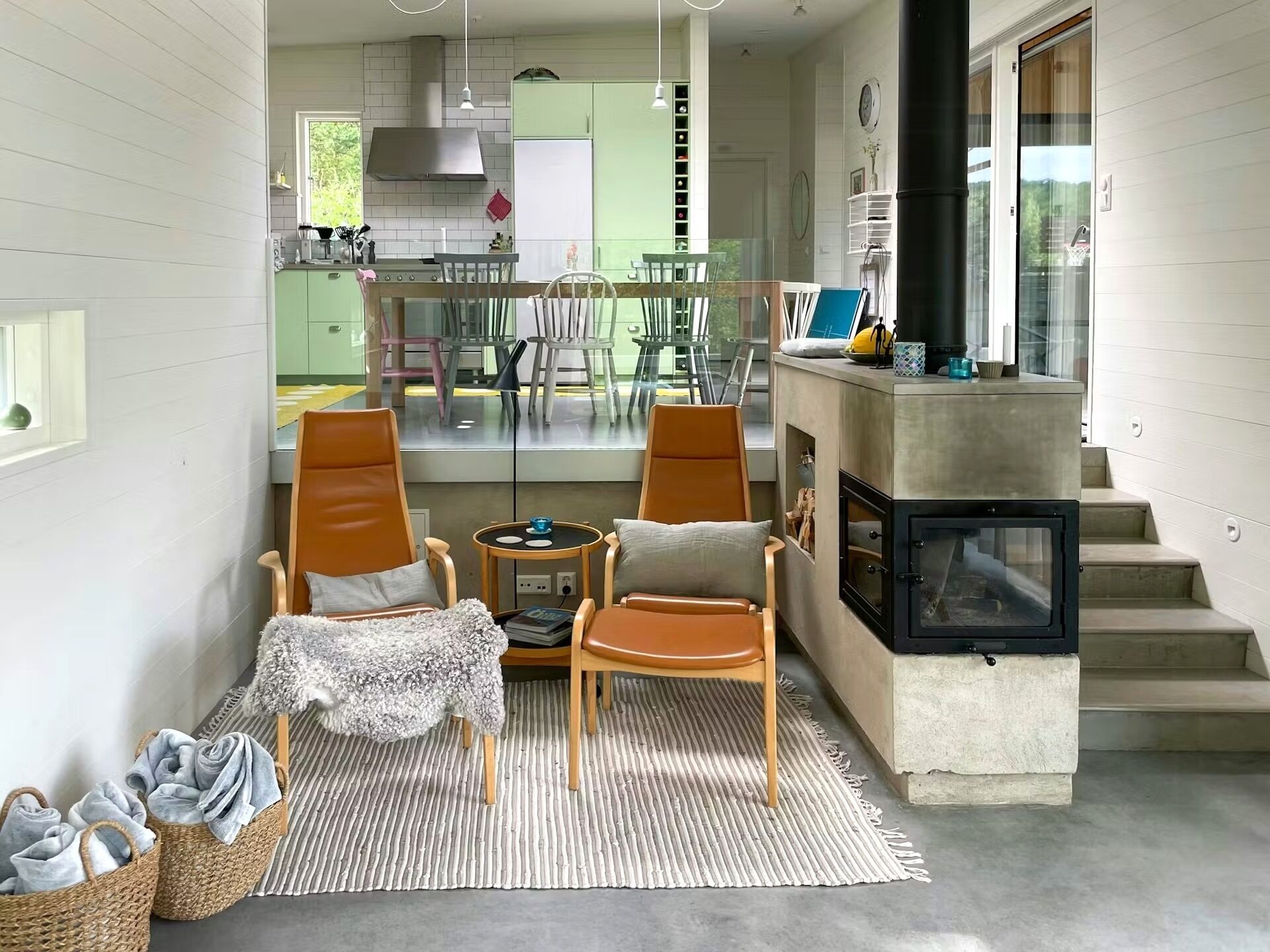 Ein gemütliches Wohnzimmer mit Kamin, eine Essecke mit Stühlen und eine durchgehende Tür sichtbare Küche.