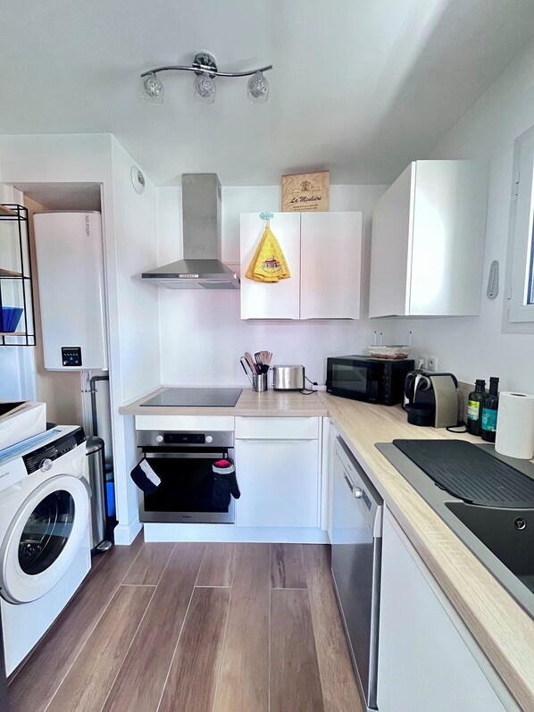 Une cuisine compacte équipée d’un lave-linge, d’un four, d’un four à micro-ondes et d’un petit plan de travail.