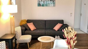 A living room with a sofa, chairs, a small table, a lamp, a painting, and a vase with flowers. - Arcachon: Bright apartment with a balcony, just 1 minute from the beach (Arcachon)