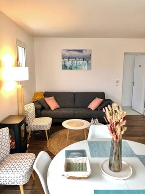 Ein Wohnzimmer mit einer Couch, Sesseln, einem kleinen Tisch, einer Lampe, einem Gemälde und einer Vase mit Blumen.